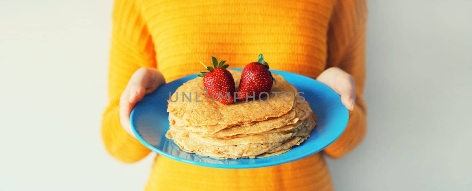 Cooking, close up woman housewife holding plate with stack of pancakes with strawberries