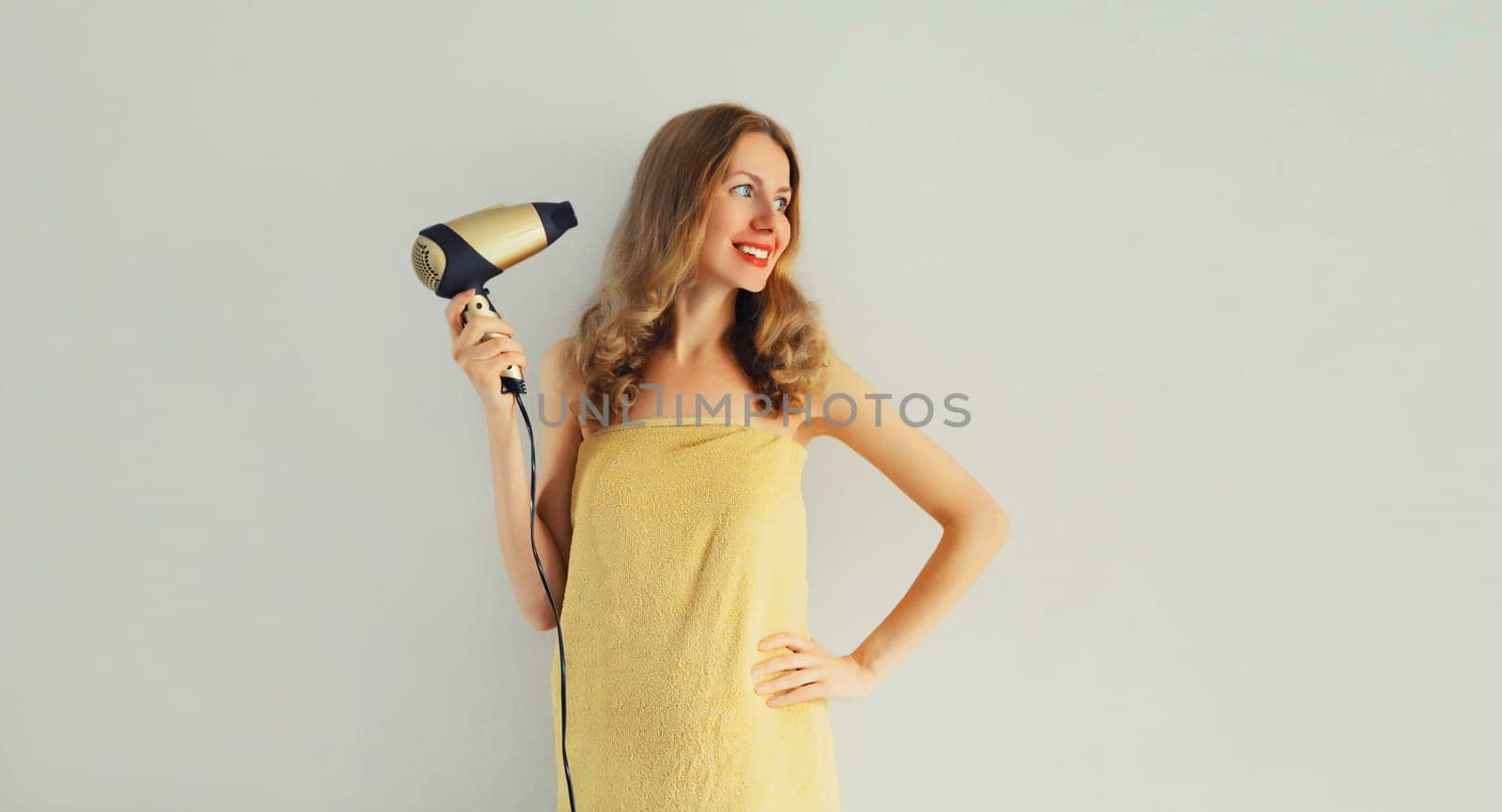Portrait of happy smiling young woman drying wet hair in wrapped bath towel after taking a shower