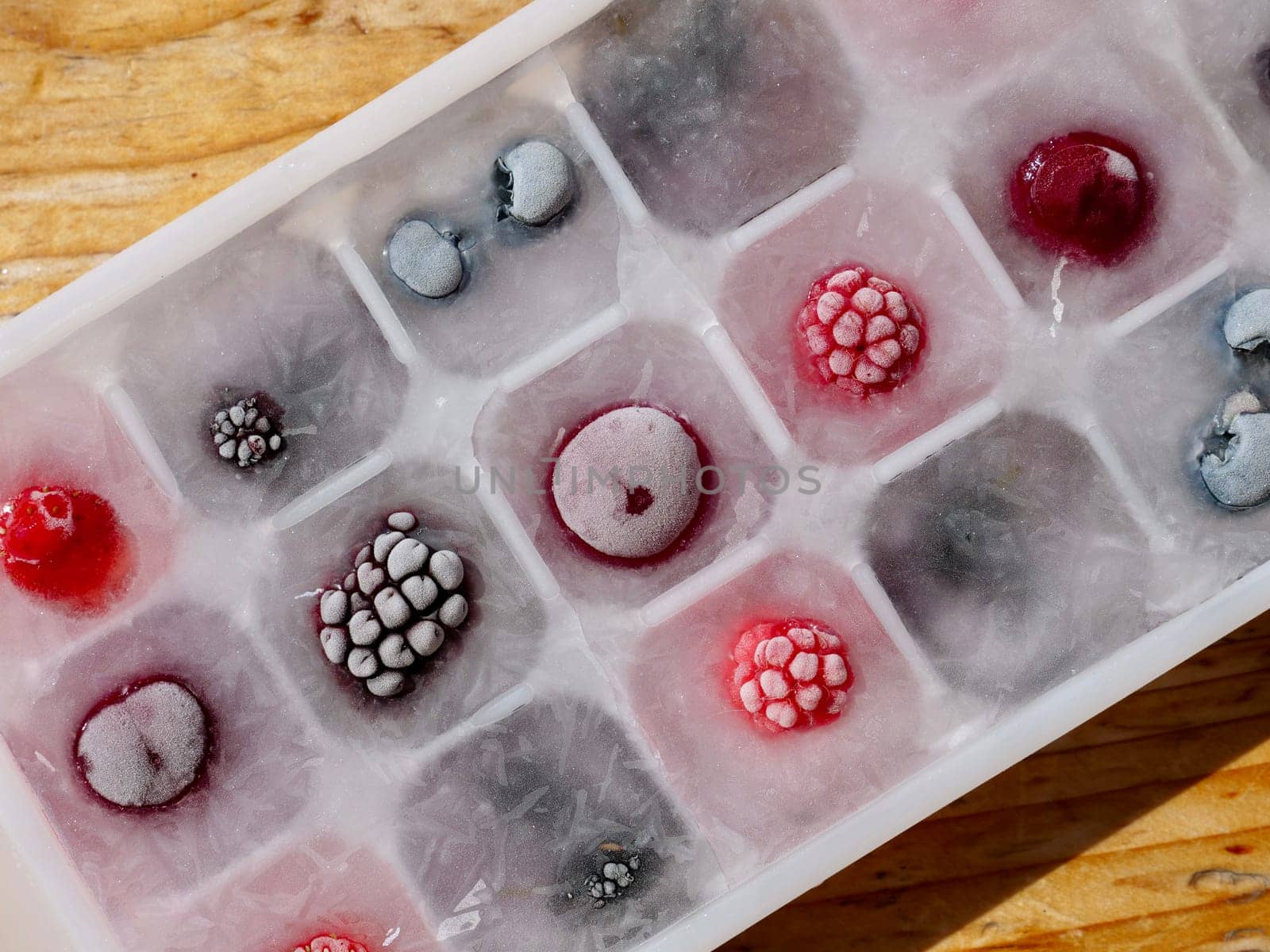 Frozen ice with berries in a container by the piece for making refreshing drinks or preserving vitamins and minerals seasonal cherries, raspberries, strawberries, blackberries, mulberries, blueberries