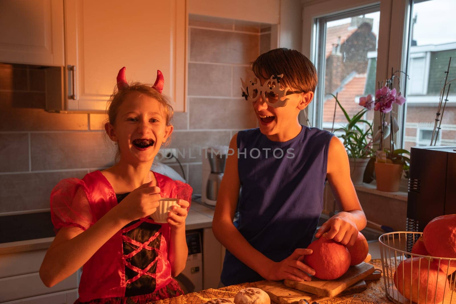 girl tasting bun filling, she and her brother dressed in halloween costumes, enjoying holiday treats in decorated dark kitchen, warm cozy atmosphere, festive mood,
