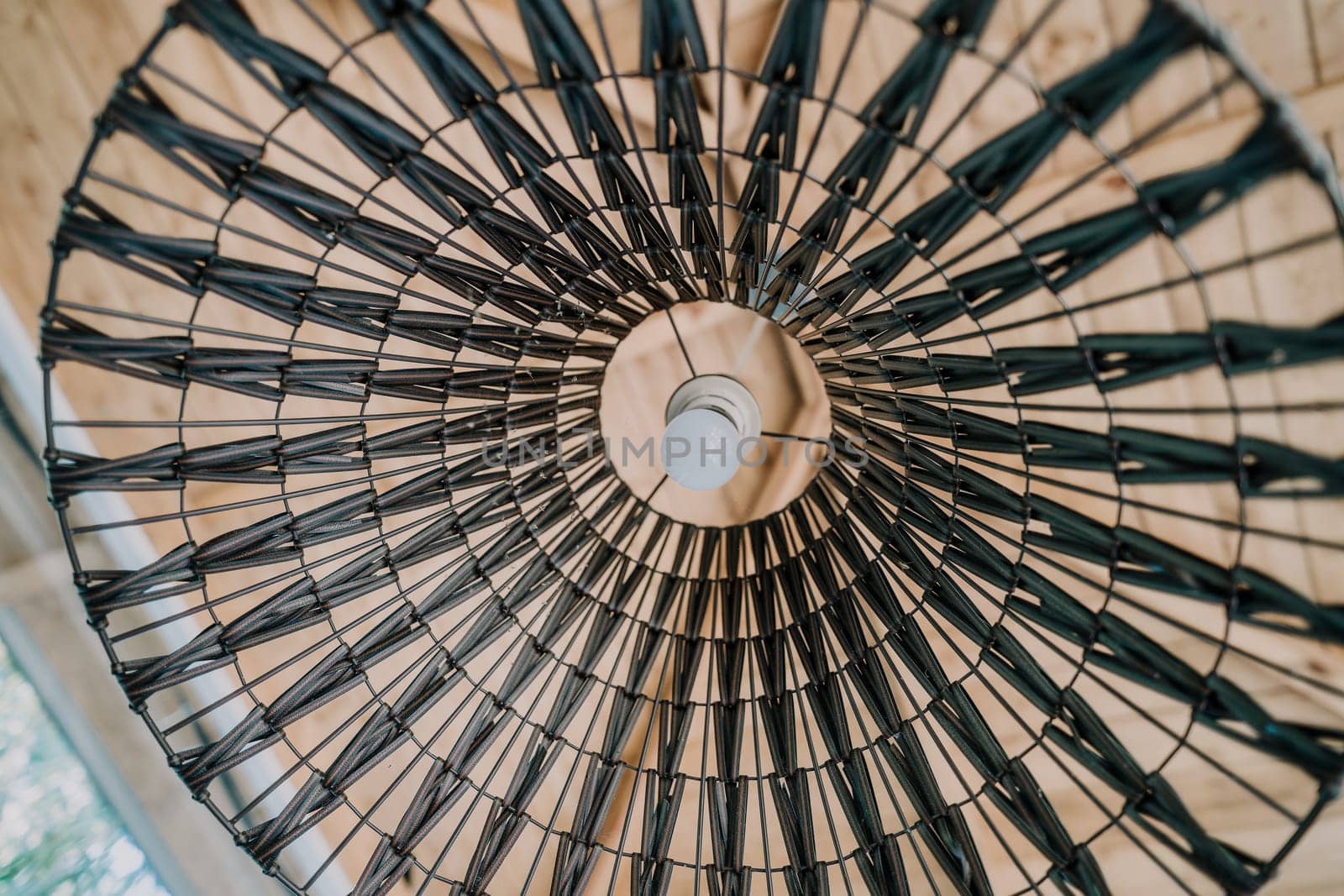 Close up of a wicker lamp shade with a light bulb inside, creating a geometric pattern.