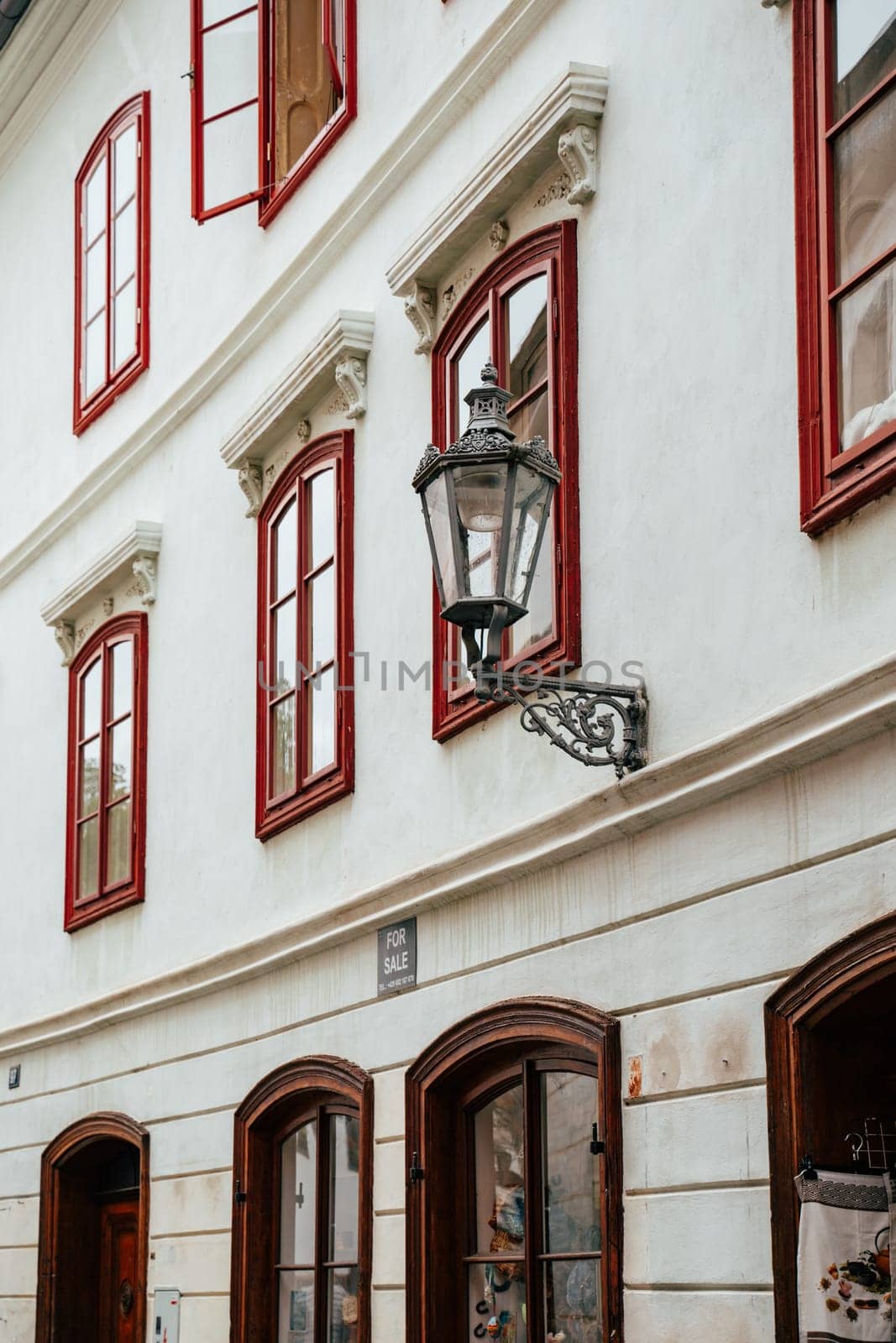 This location features a beautiful historic building adorned with striking red windows and a vintage lantern. The architecture reflects classic European design elements, inviting viewers to explore the quaint street where the building is situated.