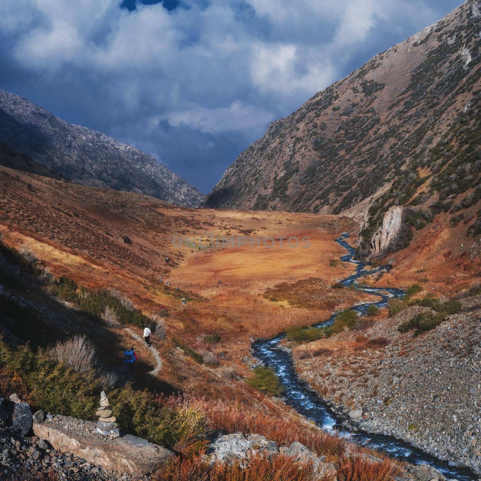landscape with a group of tourists traveling people in an autumn orange valley with a river stream in the mountains in fall