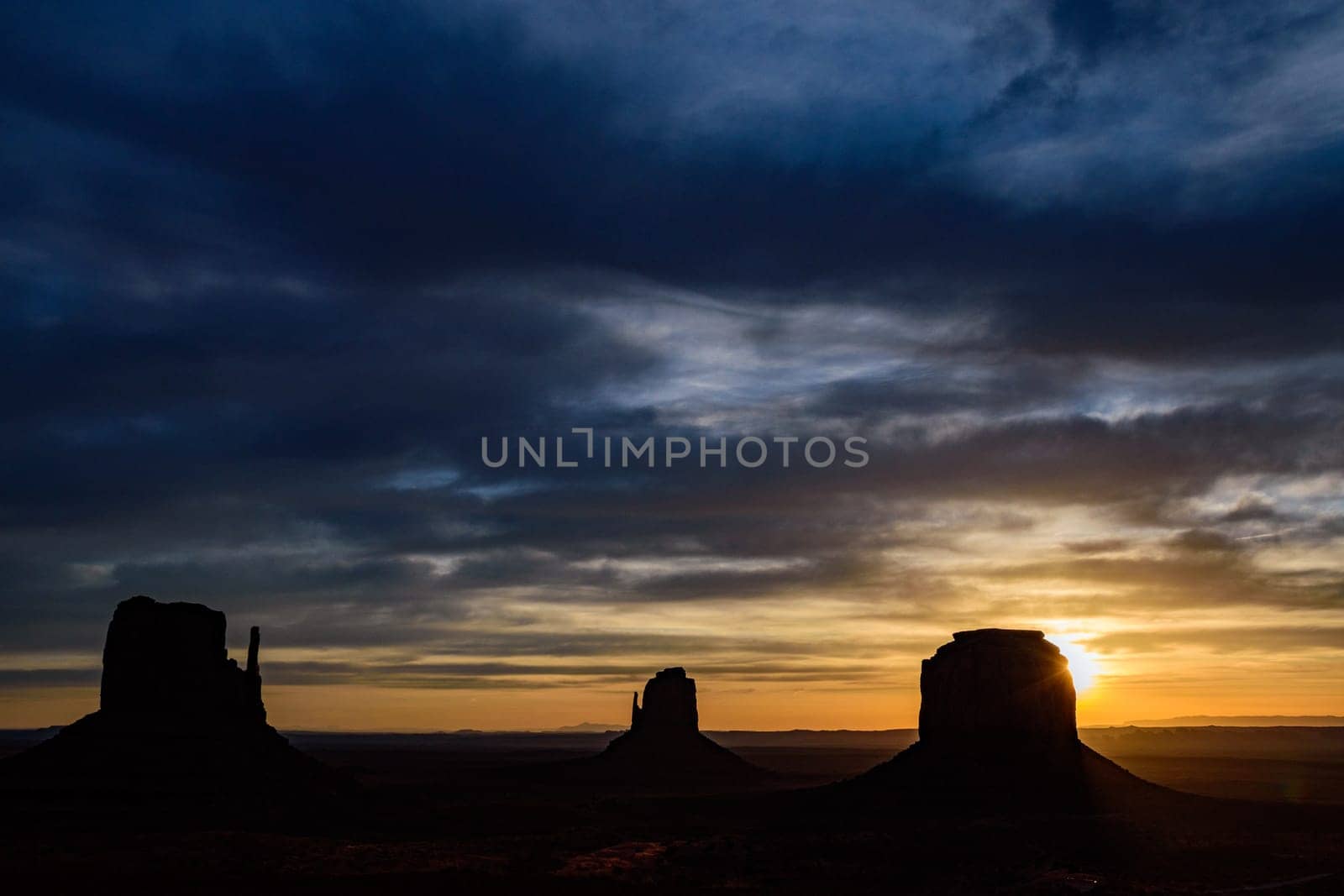 Captivating sunrise at Monument Valley, showcasing the iconic Mittens and Merrick Butte in silhouette. The lens flare adds a dramatic touch to the morning sky, highlighting the beauty of Arizona, USA.