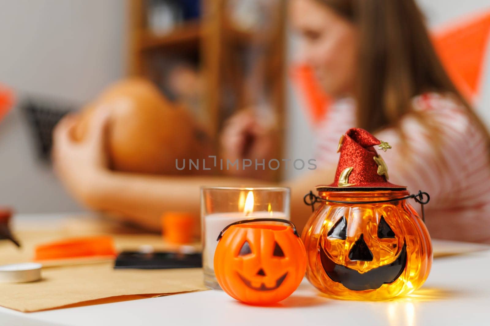 Woman in striped shirt creating Halloween pumpkin lantern on decorated table with candle and accessories. Studio craft session.