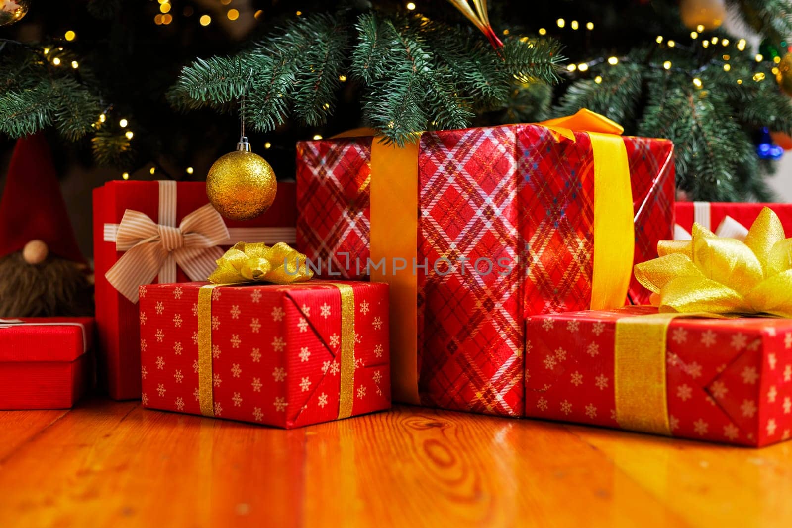 Red and gold wrapped Christmas gifts under a decorated tree with lights. Holiday season and gift-giving concept for design.