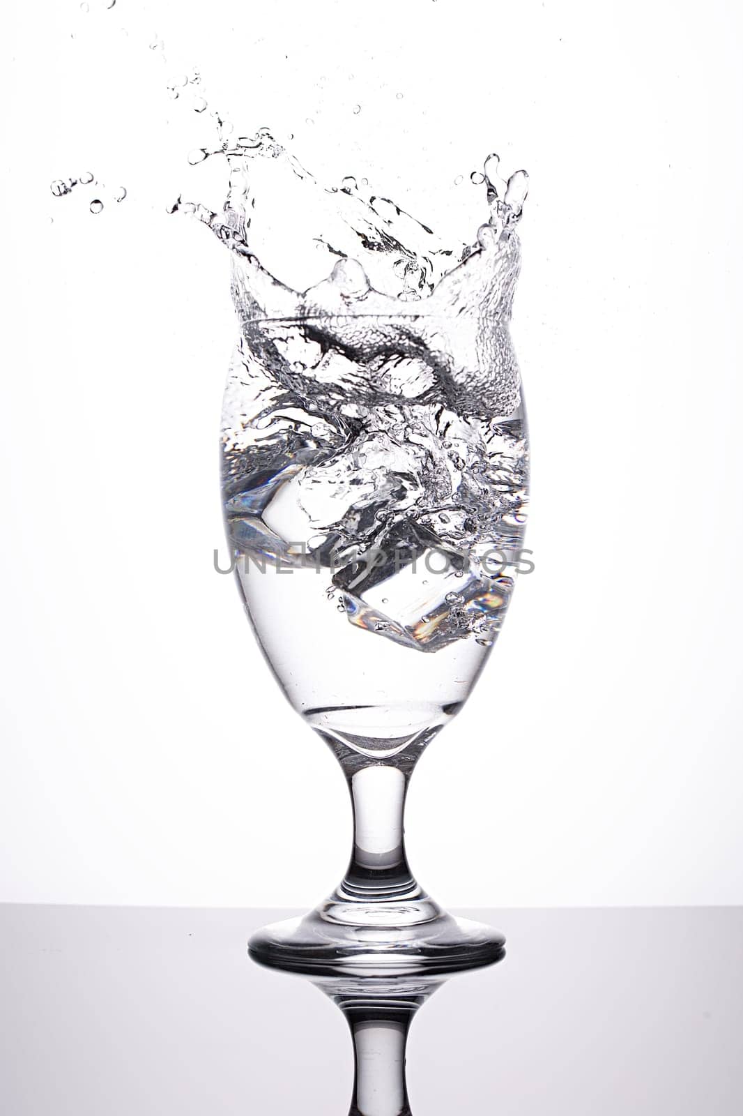 A studio photo of ice being dropped into a glass of water against a white background.