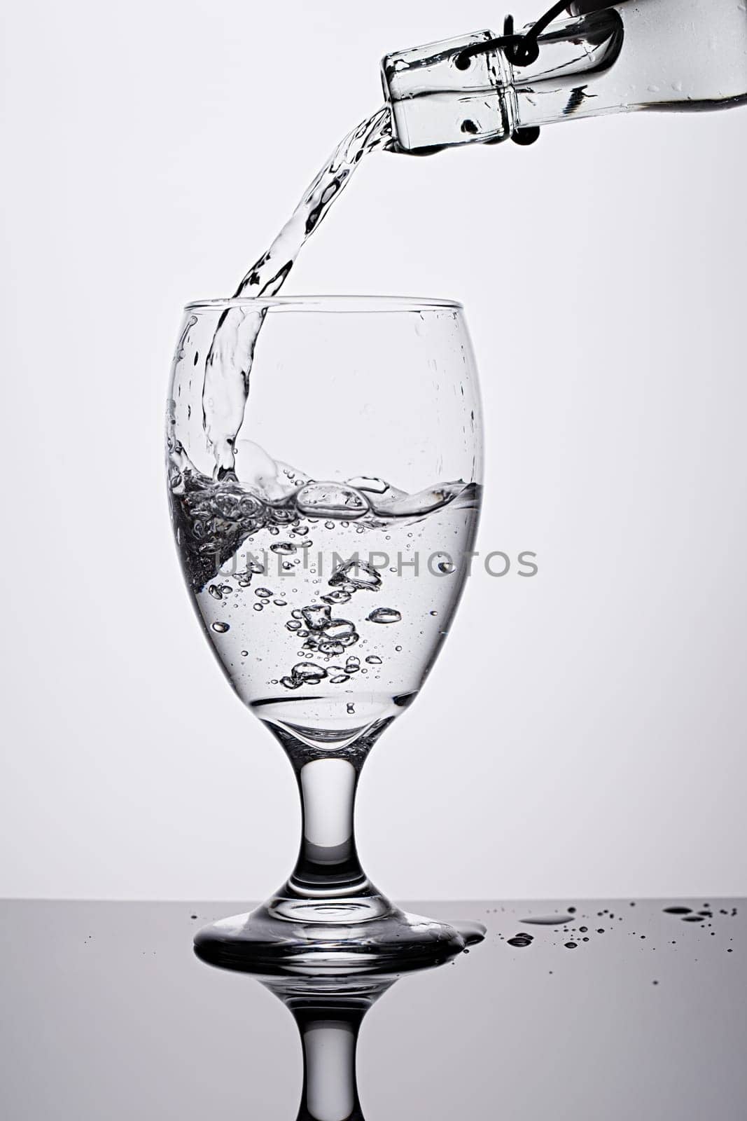 A studio photo of pouring water from a bottle into a glass against a white background.
