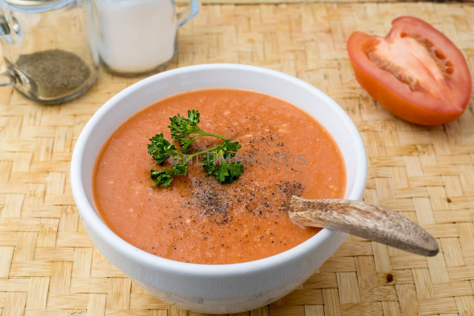 A studio photo of a bowl of homemade tomato soup with parsley and salt and pepper shakers.