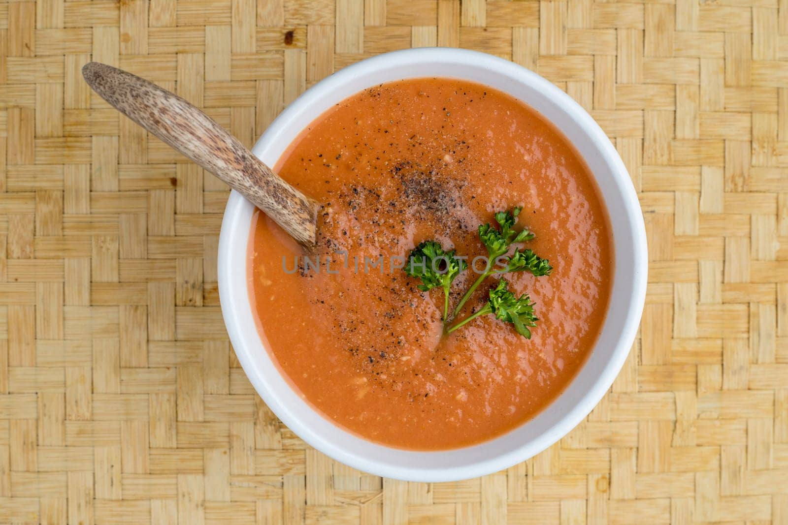 A studio overview photo of a bowl of tomato soup with a sprig of parsley on top.