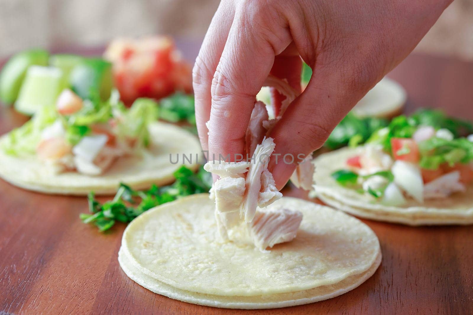 Putting pieces of chicken on a small street taco on a wooden board.