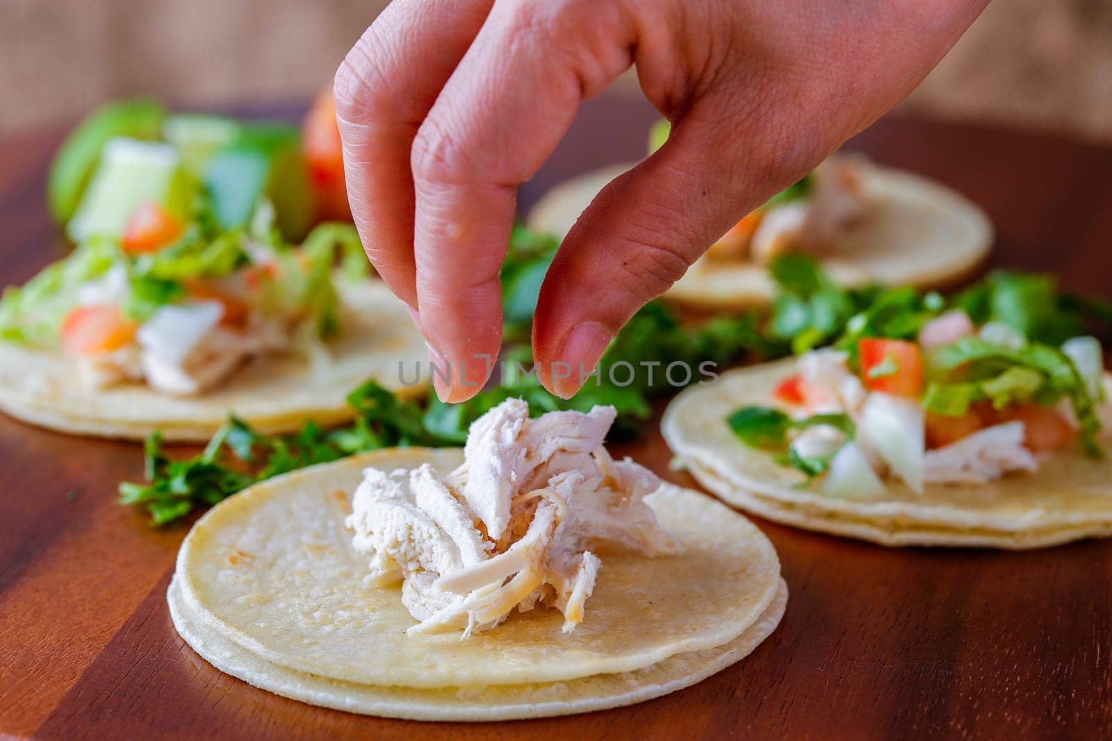 Putting pieces of chicken on a small street taco on a wooden board.