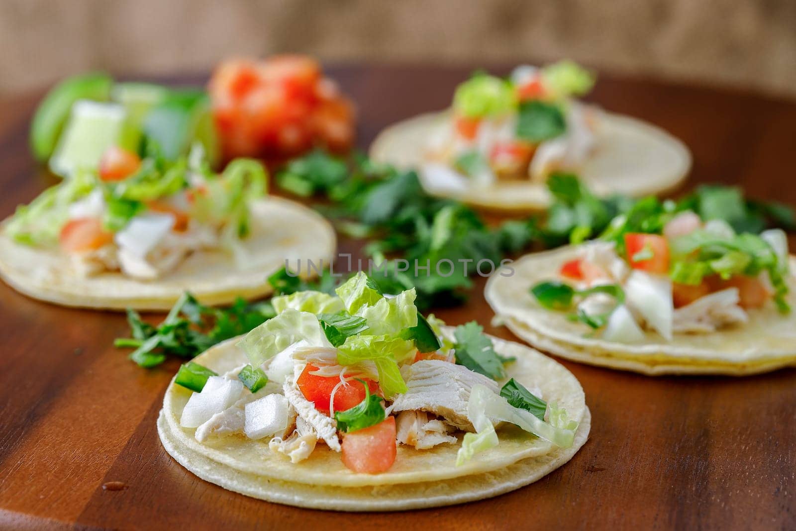A close up photo of four street tacos displayed on a wooden board.