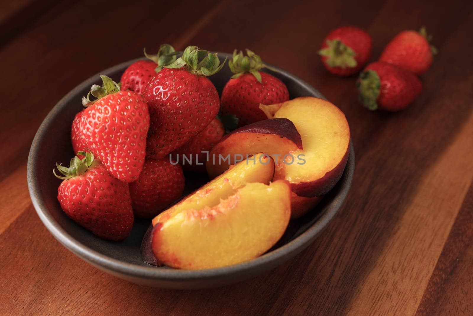 A studio photo of a bowl of fresh strawberries and sliced peaches.