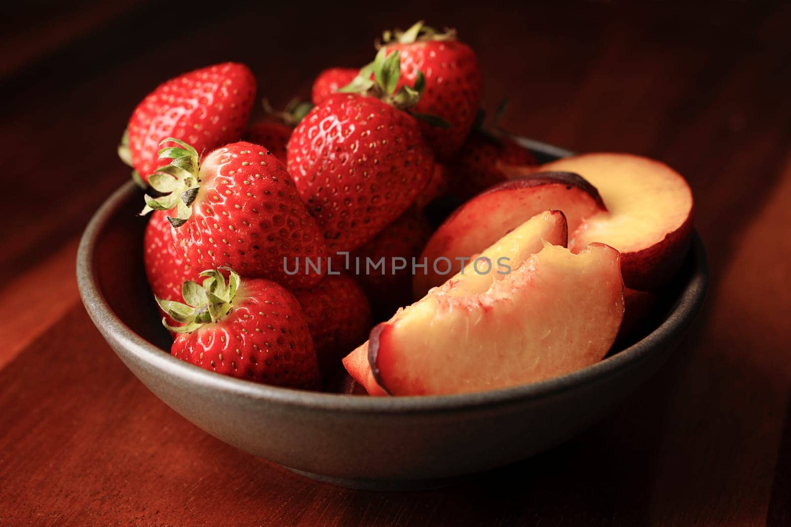 A studio photo of a bowl of fresh strawberries and sliced peaches.