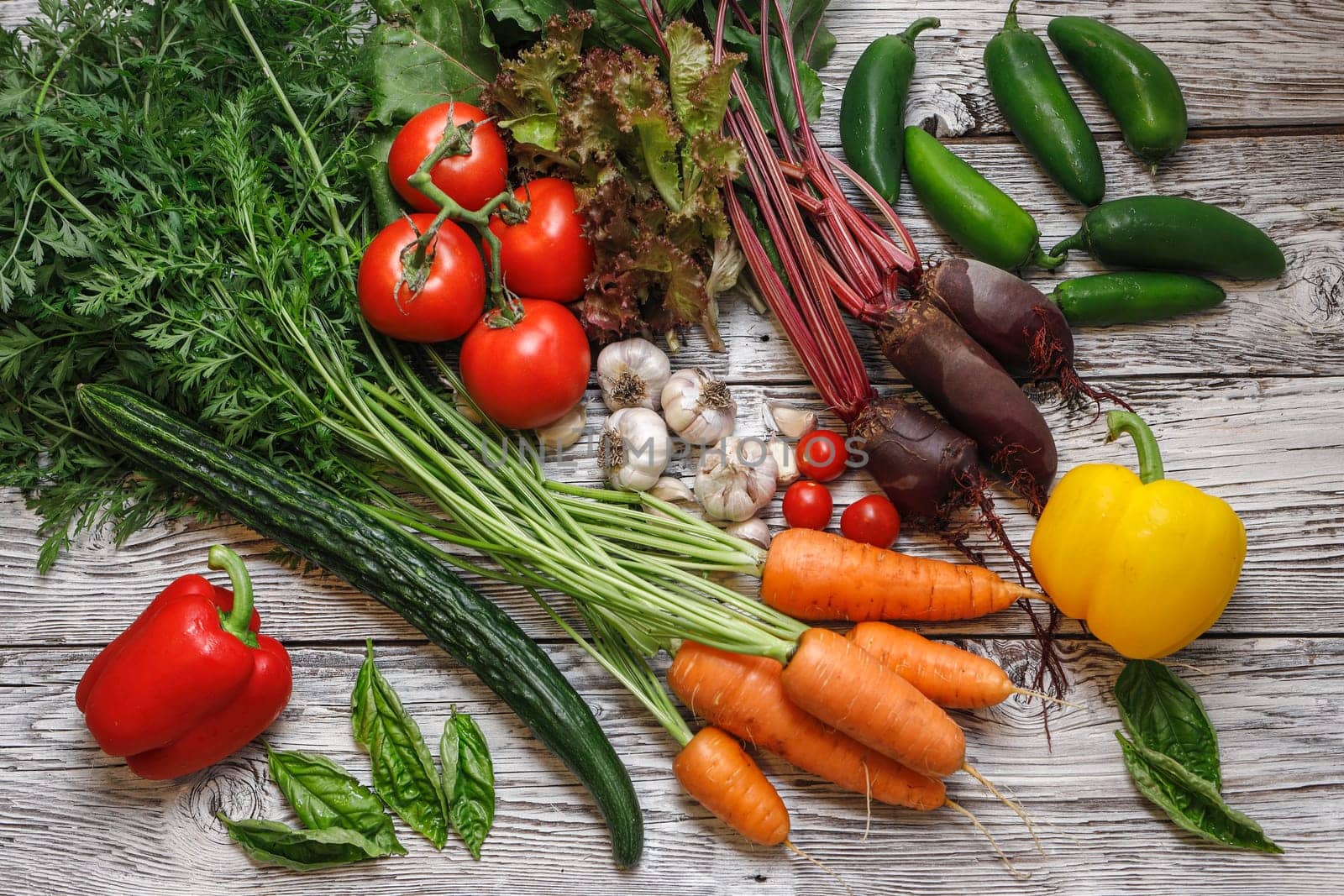An overview of assorted vegetables and basil on a wooden table.