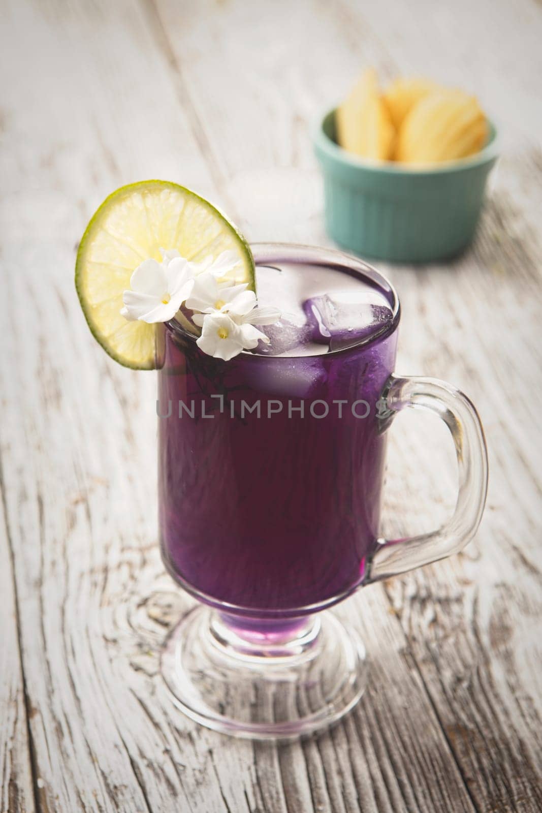 A refreshing glass of butterfly pea flower tea with ice and a lime.