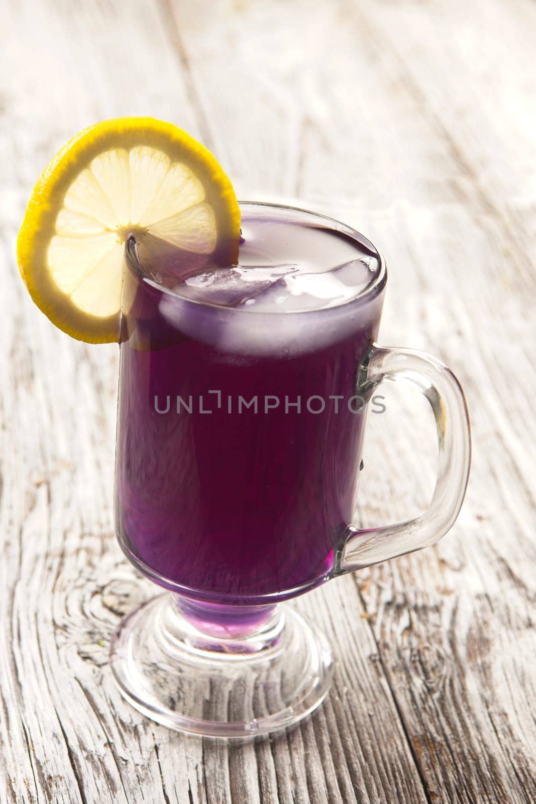 A refreshing glass of butterfly pea flower tea with ice and a lemon slice.