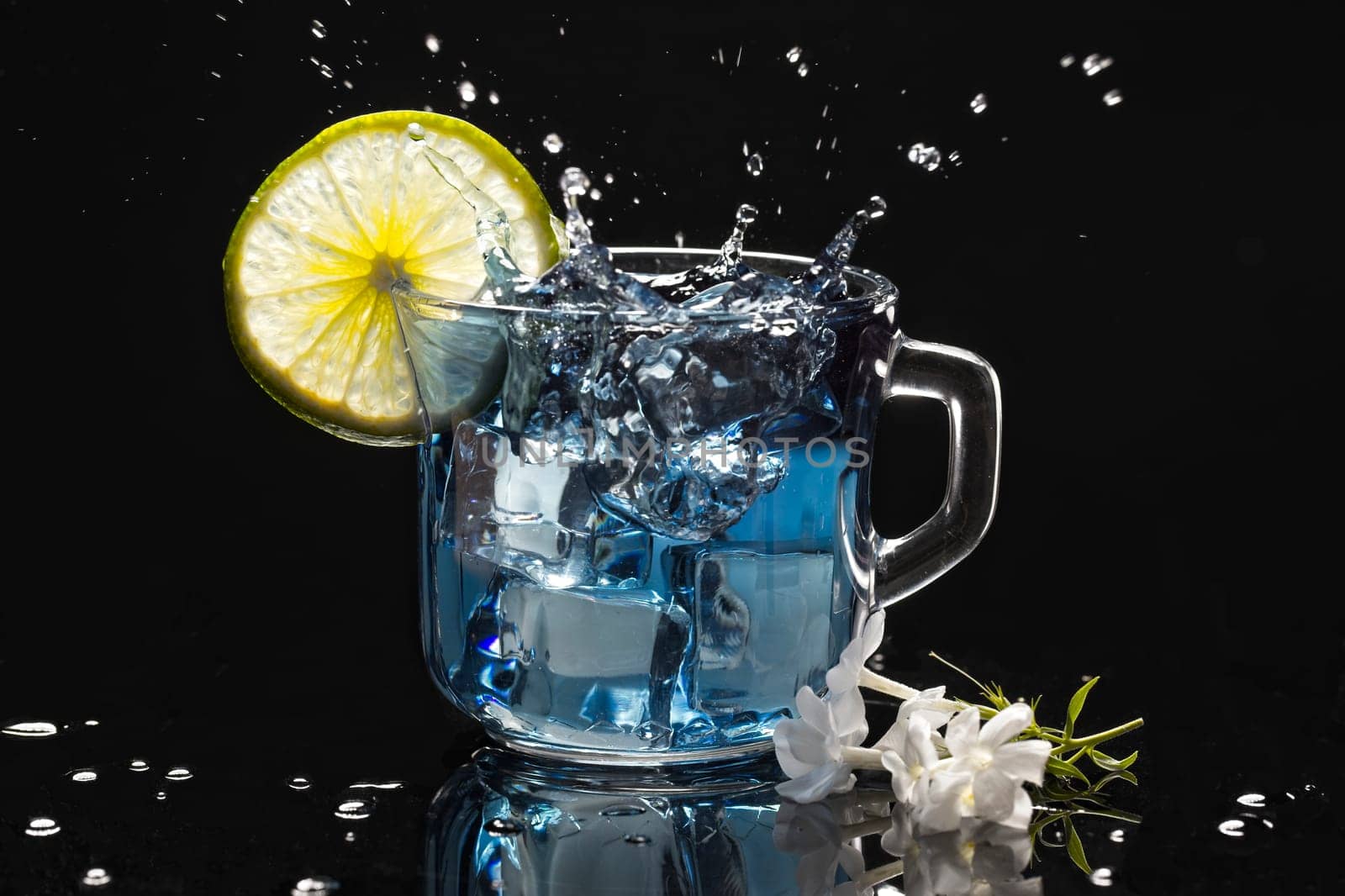 Ice cube splashing into a cup of butterfly pea flower tea with a lime slice.