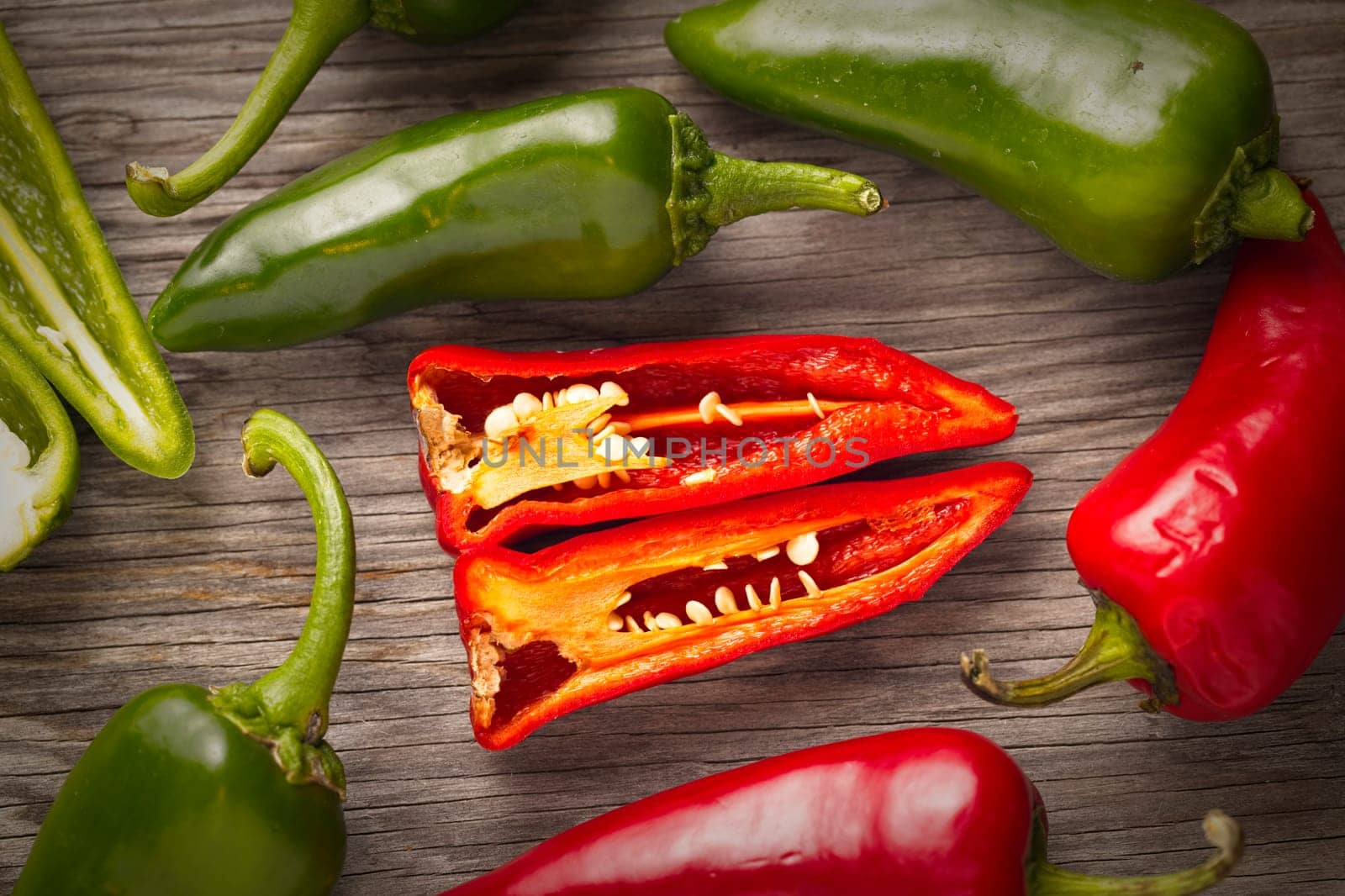 An overview of whole and sliced red and green peppers on wood.