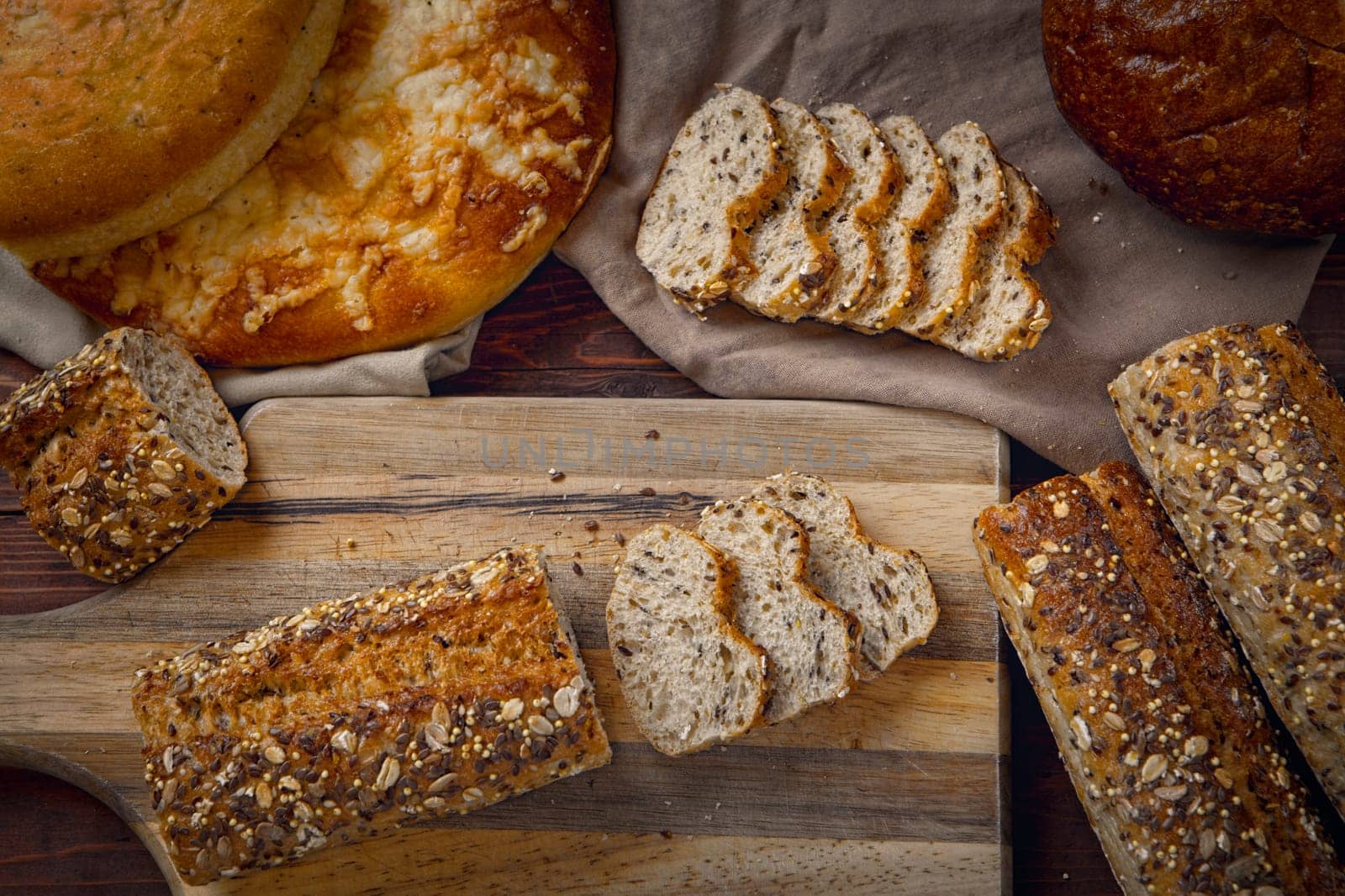 An overview of a baguette on a cutting board surrounded by various types of breads.