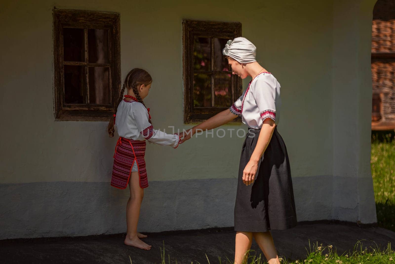 In front of a house, a woman and a little girl joyfully hold hands, possibly enjoying a special event. The scene captures happiness and warmth
