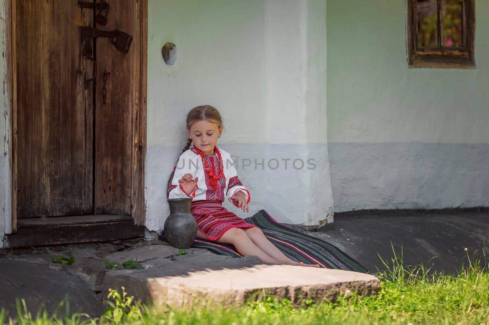 A lovely girl dressed in her colorful traditional clothing is sitting by a charming door on a bright sunny day