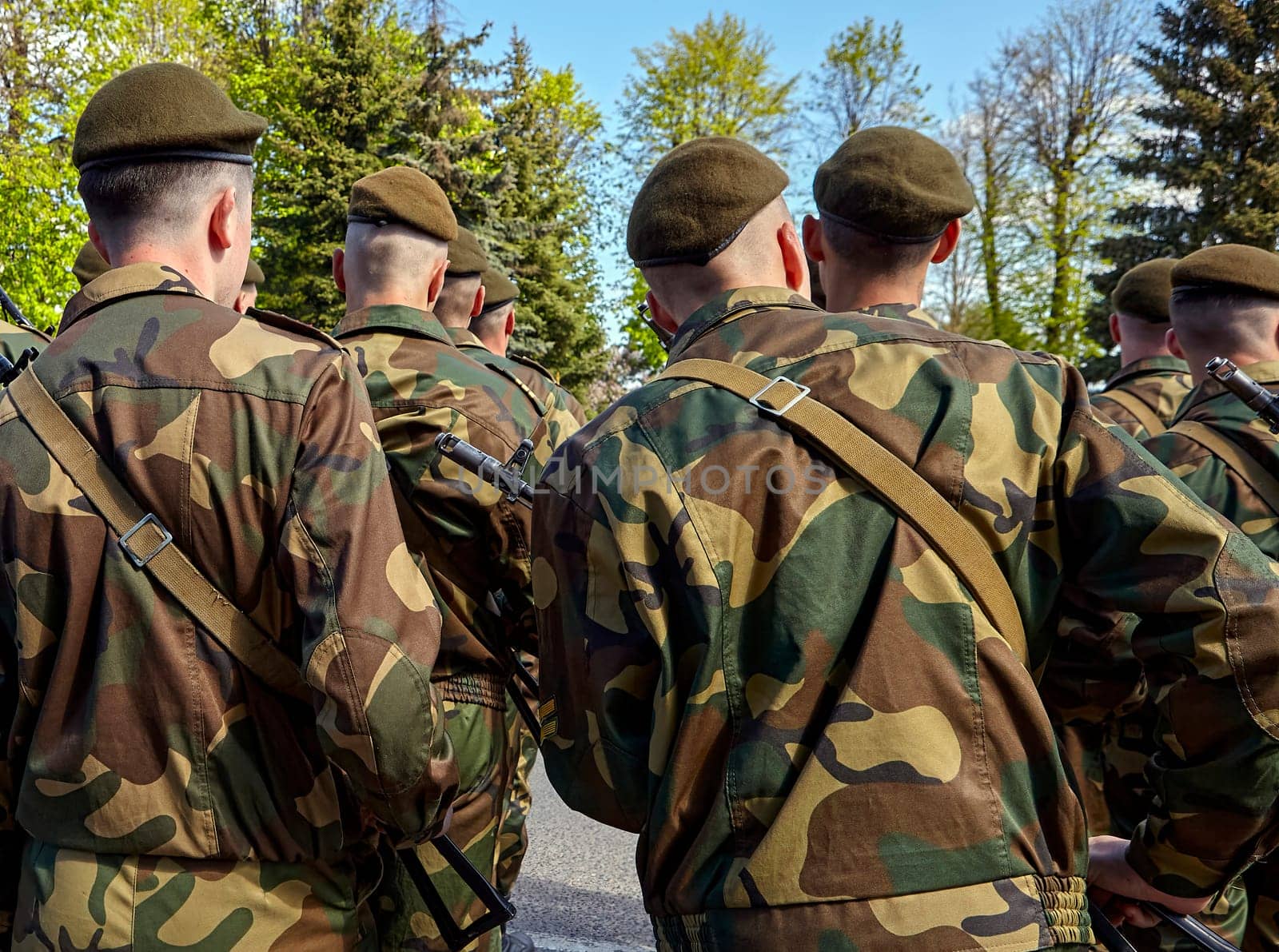 Soldiers in camouflage uniforms walk together through a wooded area, preparing for a military training activity on a sunny day.
