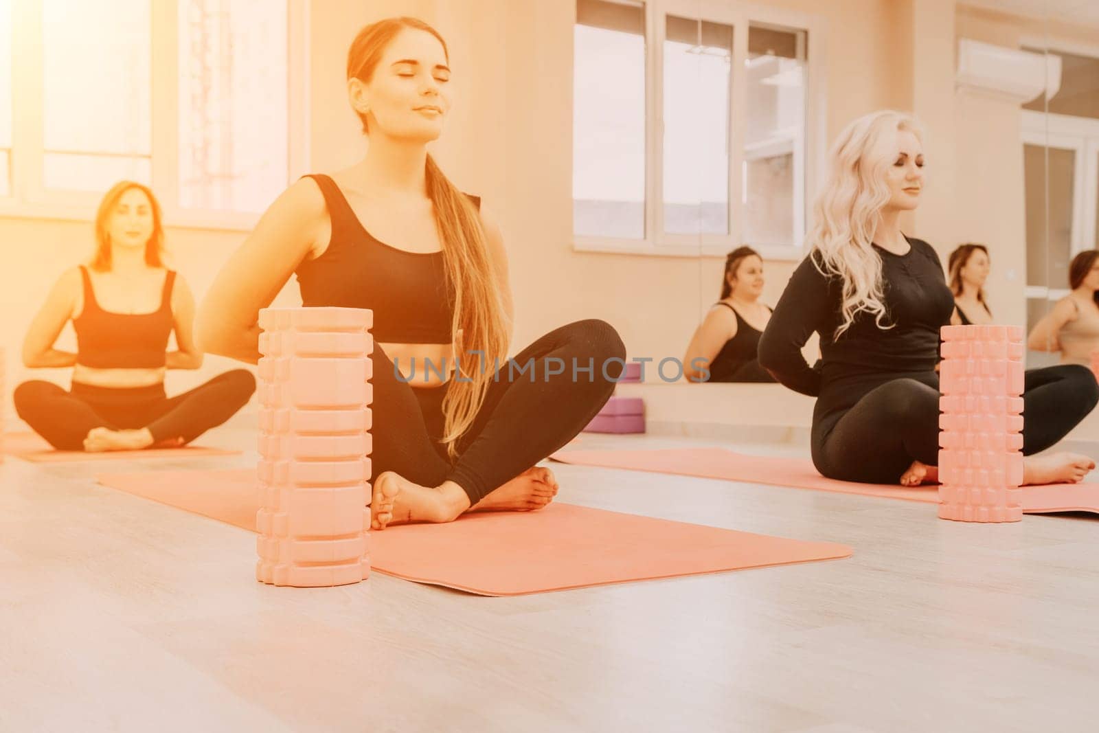 Middle aged well looking women, performing fascia exercises on the floor using a massage foam roller - tool to relieve tension in the back and relieve muscle pain. Female fitness yoga routine concept by panophotograph