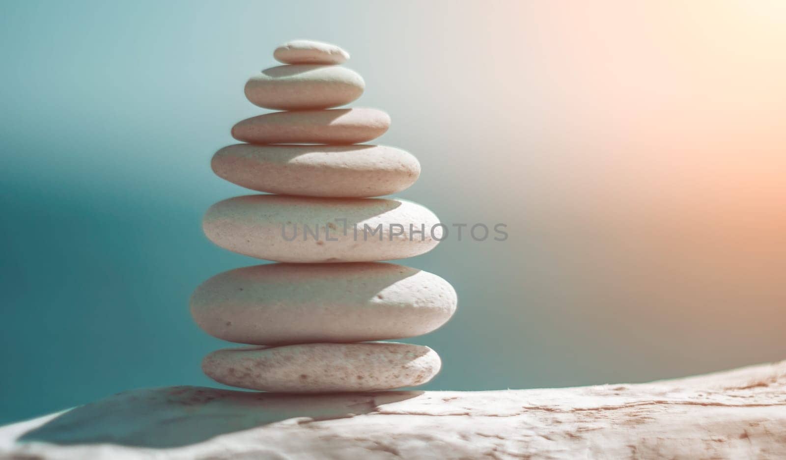 Balanced rock pyramid on sea pebbles beach, sunny day and clear sky at sunset. Golden sea bokeh on background. Selective focus, zen stones on sea beach, meditation, spa, harmony, calm, balance concept by panophotograph