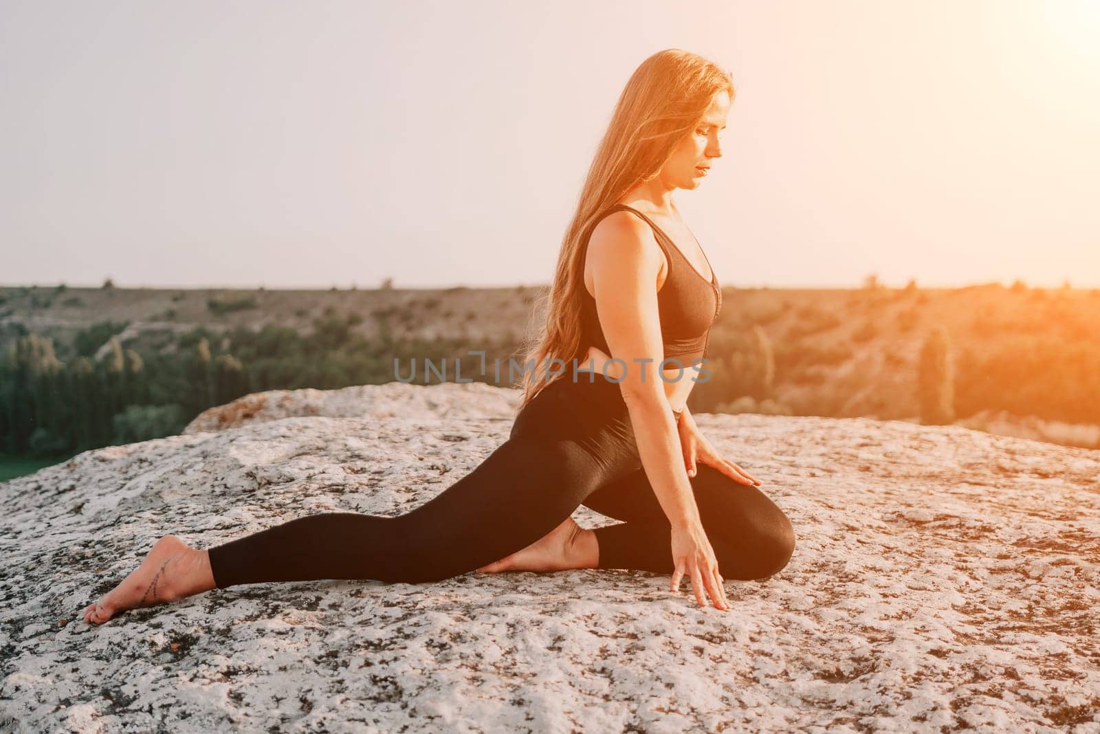 Well looking middle aged woman with long hair, fitness instructor in leggings and tops doing stretching and pilates on the rock near forest. Female fitness yoga routine concept. Healthy lifestyle.