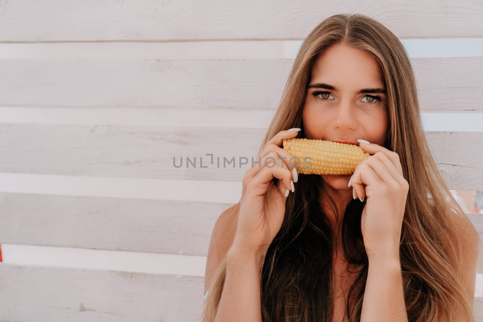 Healthy vegetarian hipster woman in summer outfit eat grilled corn and look to camera. Sexy lady on sea beach sunset or ocean sunrise. Travel, explore, active yoga and meditation lifestyle concept.