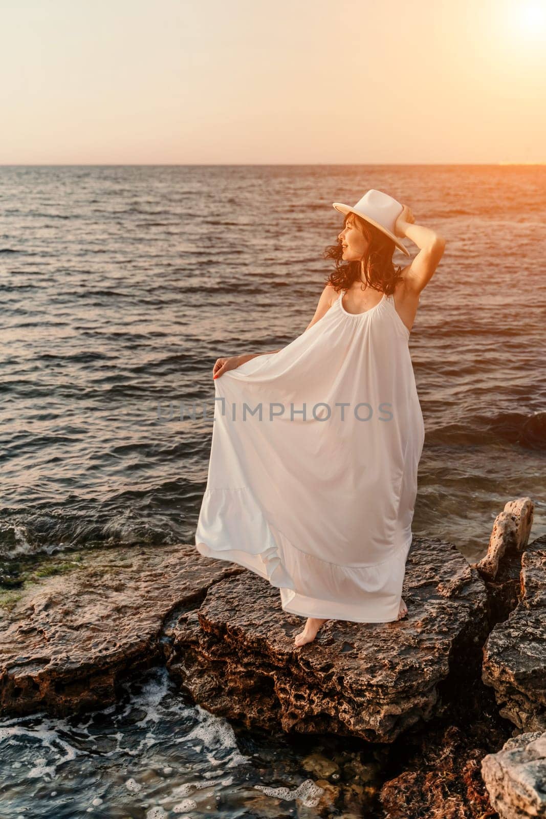 woman sea sunset. A woman in a dress, hat and with a straw bag is standing on the beach enjoying the sea. Happy summer holidays.