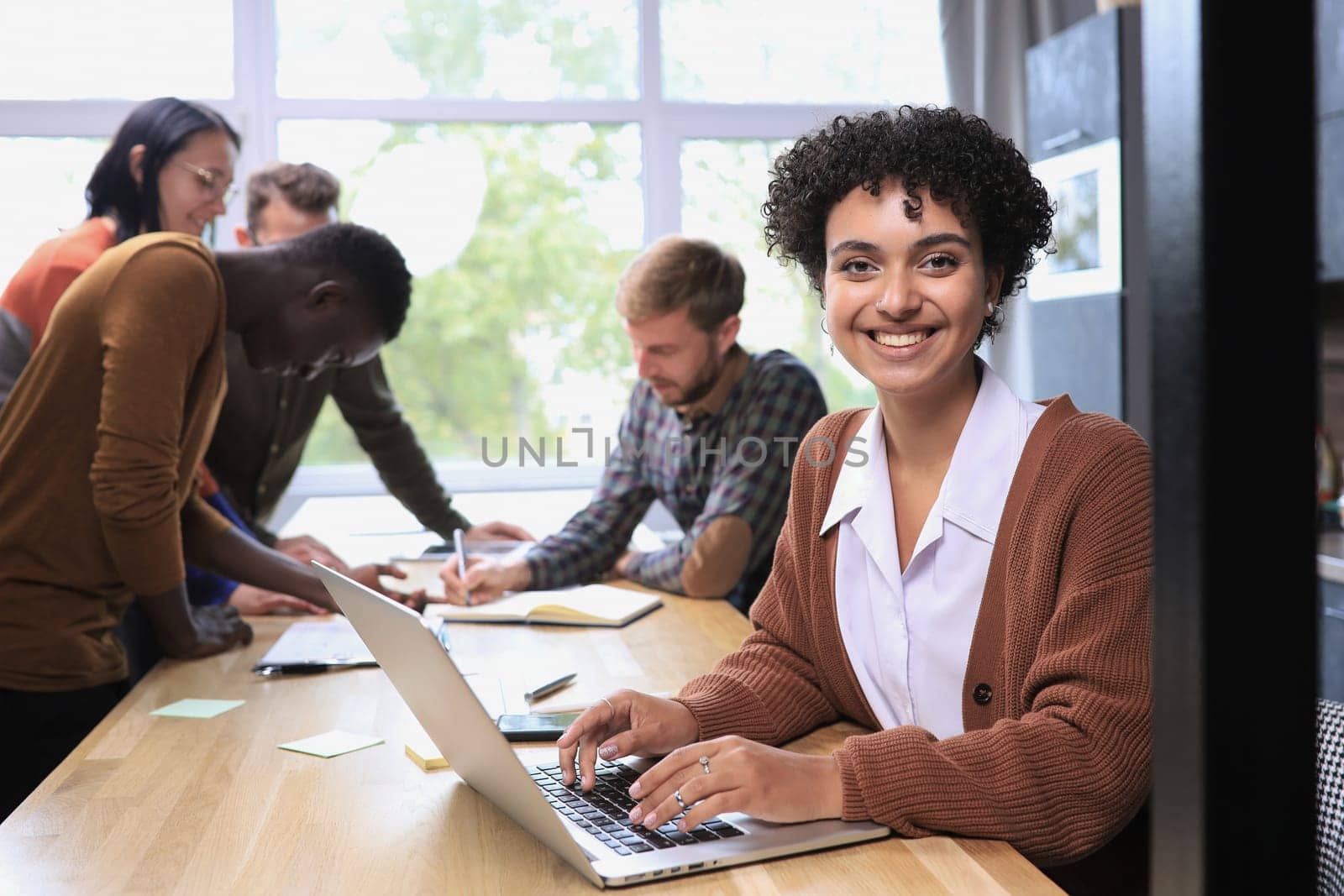 Businesswoman using laptop in office with team in background by asdf