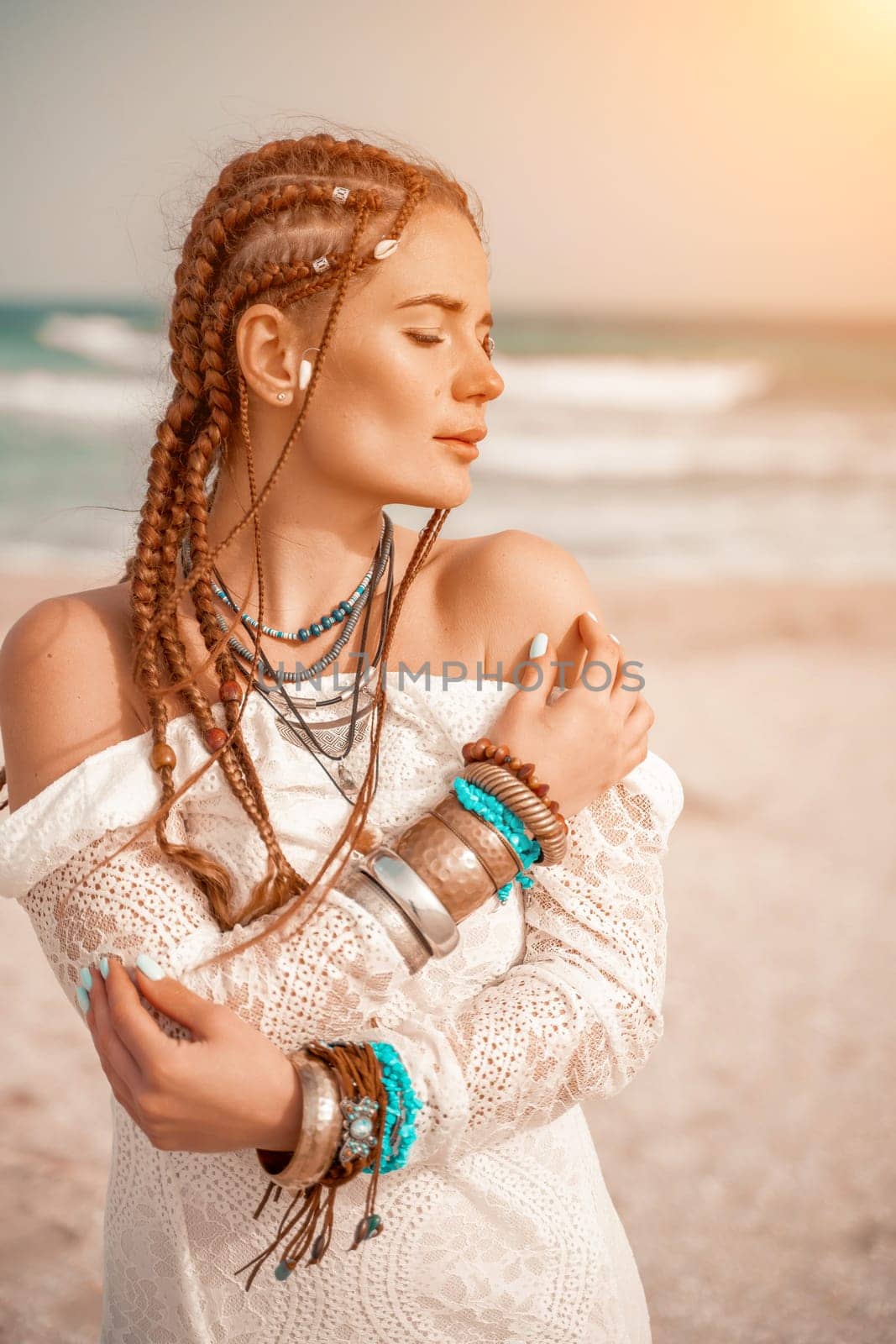 Woman portret sea white dress. Model in boho style in a white long dress and silver jewelry on the beach. Her hair is braided, and there are many bracelets on her arms