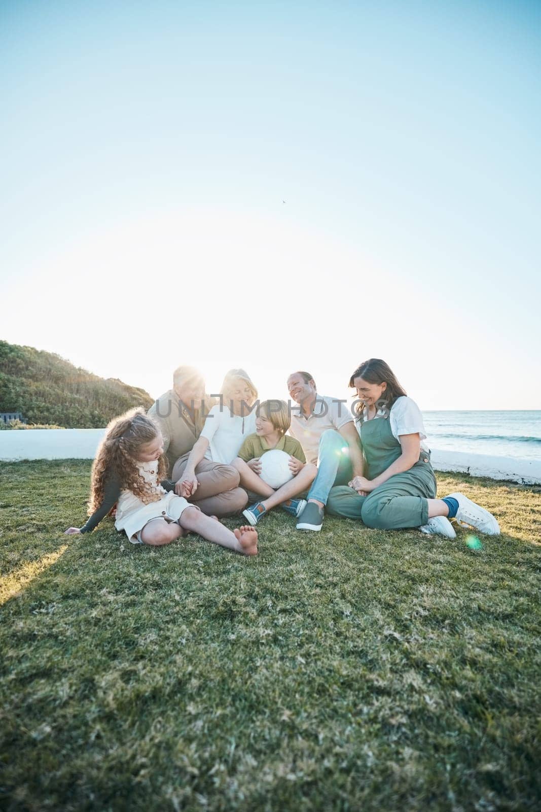Family, grandparents and kids on grass by ocean for bonding, relationship and relax together. Nature, parents and happy grandmother, grandfather and children on holiday, vacation and travel by sea.