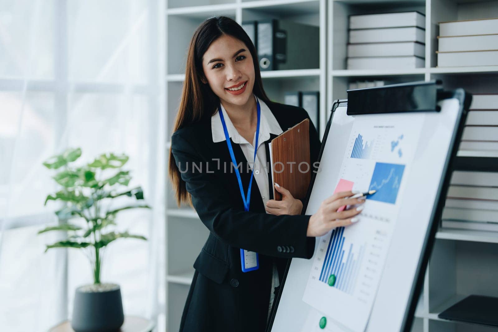 Portrait of young asian woman holding notebook with presentation of strategy, investment plan and marketing. by Manastrong