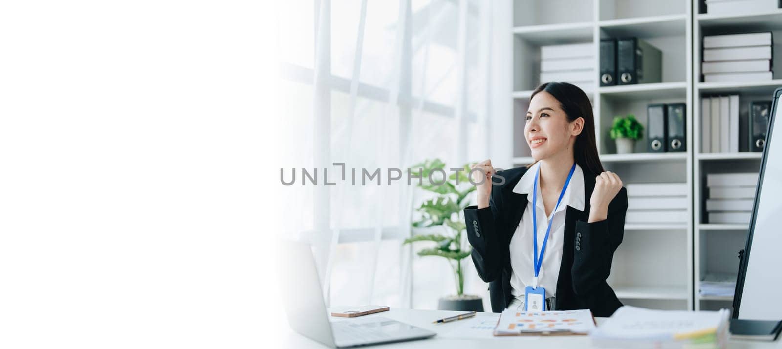 Portrait of a woman business owner showing a happy smiling face as he has successfully invested her business using computers and financial budget documents at work.