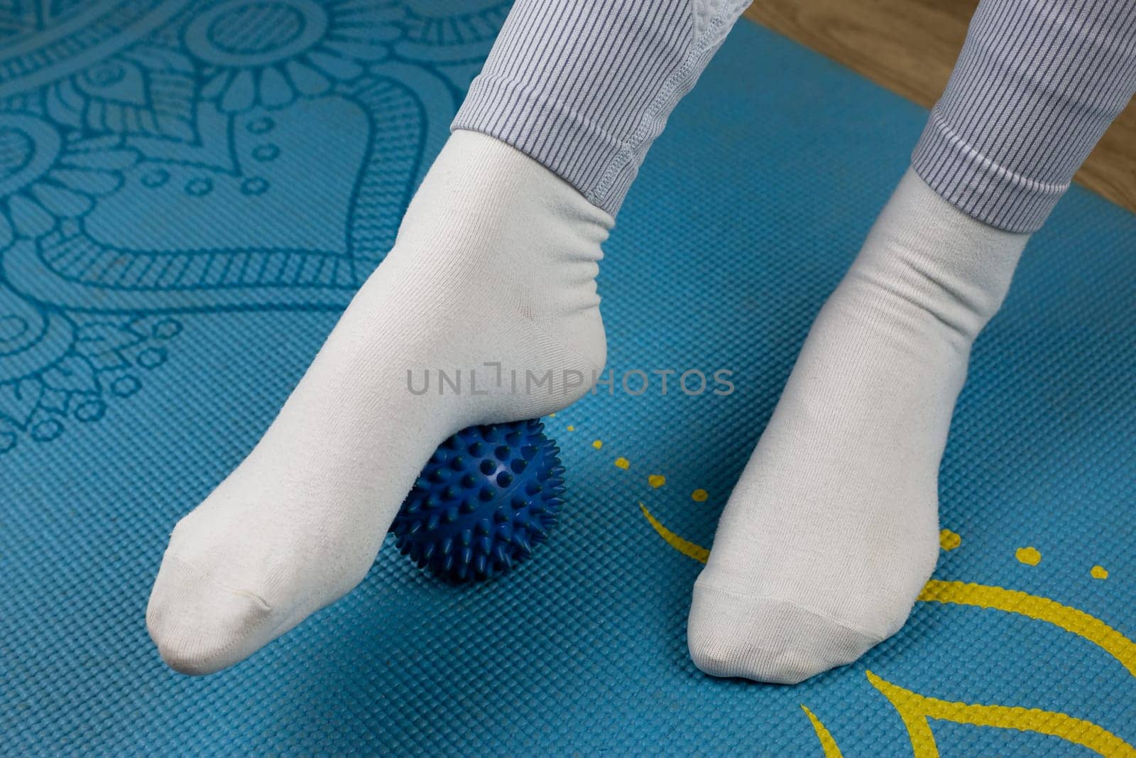 Exercise with massage ball for legs, working out muscles and relaxing massage for swelling. Rubber ball with spikes for rolling with feet during mfr. Therapeutic foot massage with special sports equipment for yoga