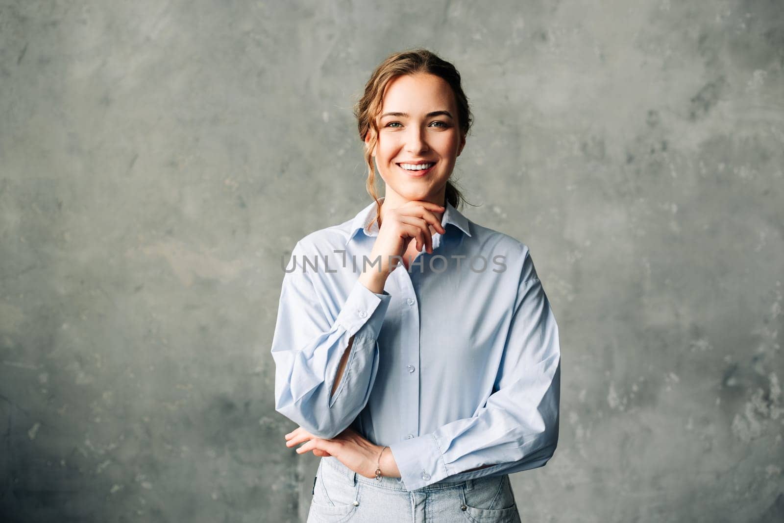 Confident young businesswoman in a blue shirt smiles warmly at the camera. Perfect for showcasing professionalism, positivity, and executive presence in a business setting