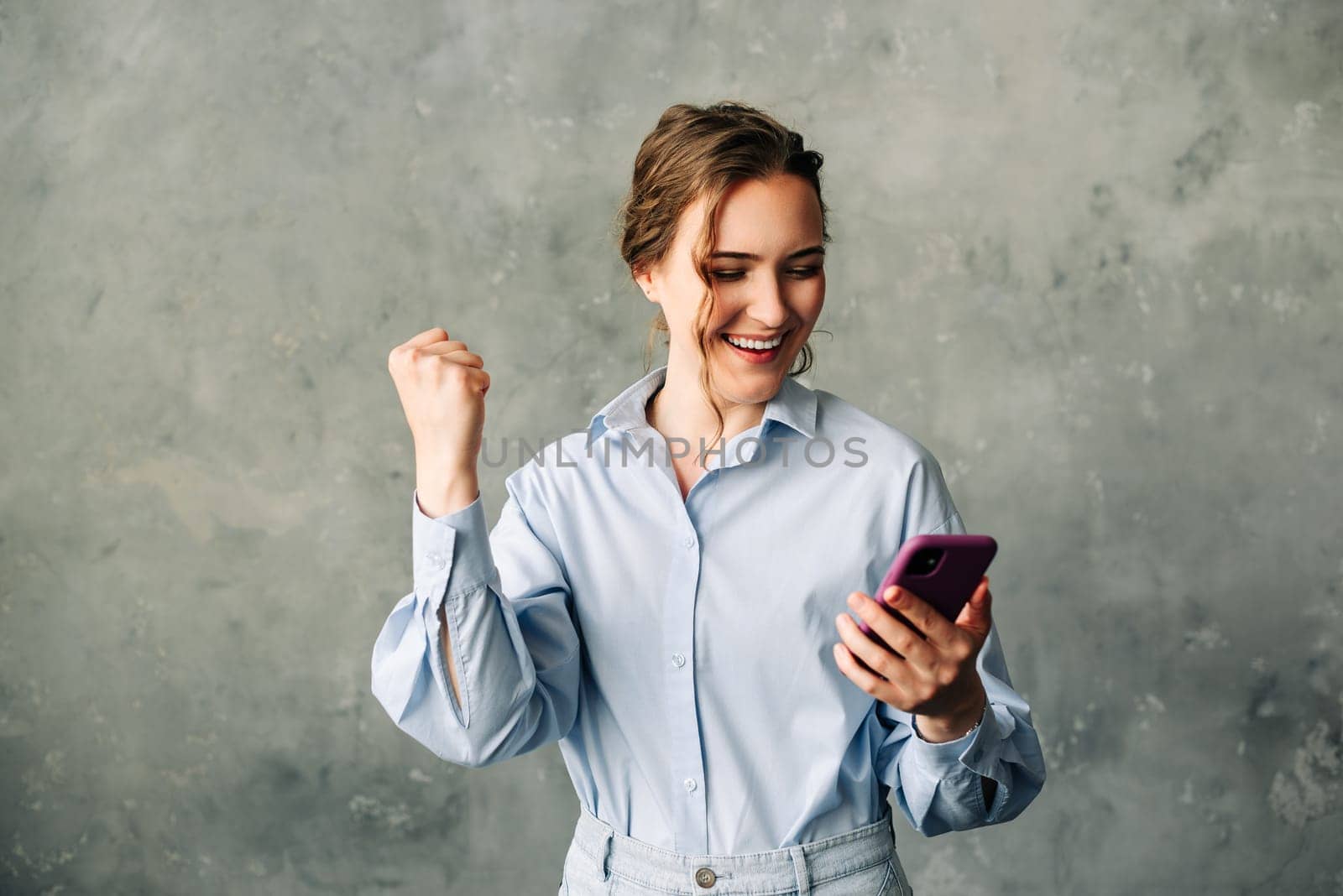 Enthusiastic young businesswoman celebrating a success or good news on her smartphone. Perfect for illustrating achievements, promotions, or positive business outcomes. Isolated on a gray background.