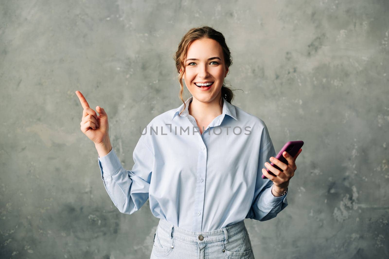 Cheerful young woman with a smartphone, enthusiastically showcasing a mobile app. Perfect for business, tech or app promotion imagery. Isolated on a neutral background. Ideal for ads and web services