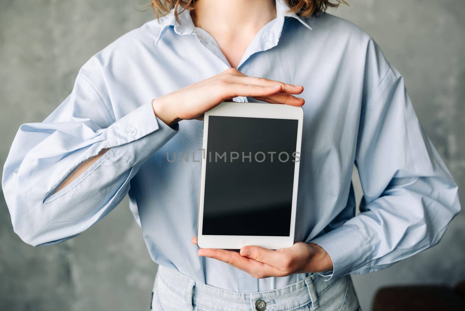 A young businesswoman is smiling as she holds a digital tablet computer which is showing a blank, empty mock-up screen. The image is advertising software, a website or web service, and it is standing.
