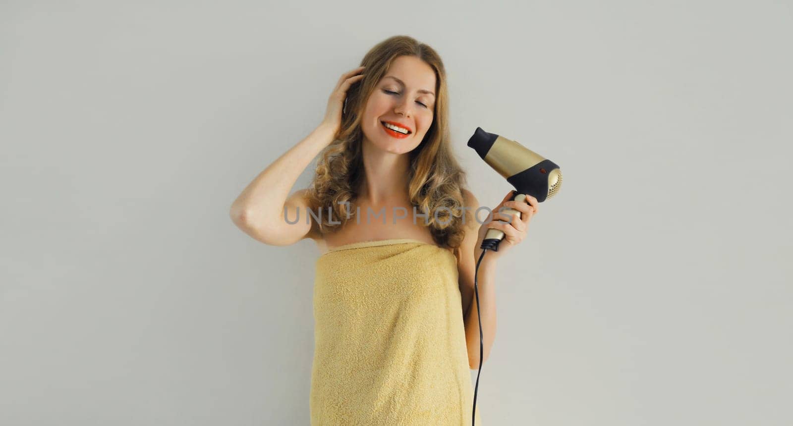 Body care, beautiful happy smiling young woman drying wet hair, she wrapped her body with bath towel after taking a shower, standing at home