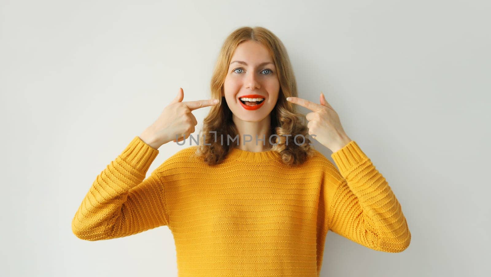 Portrait of happy smiling young woman points with fingers to her white clean teeth showing smile on white background