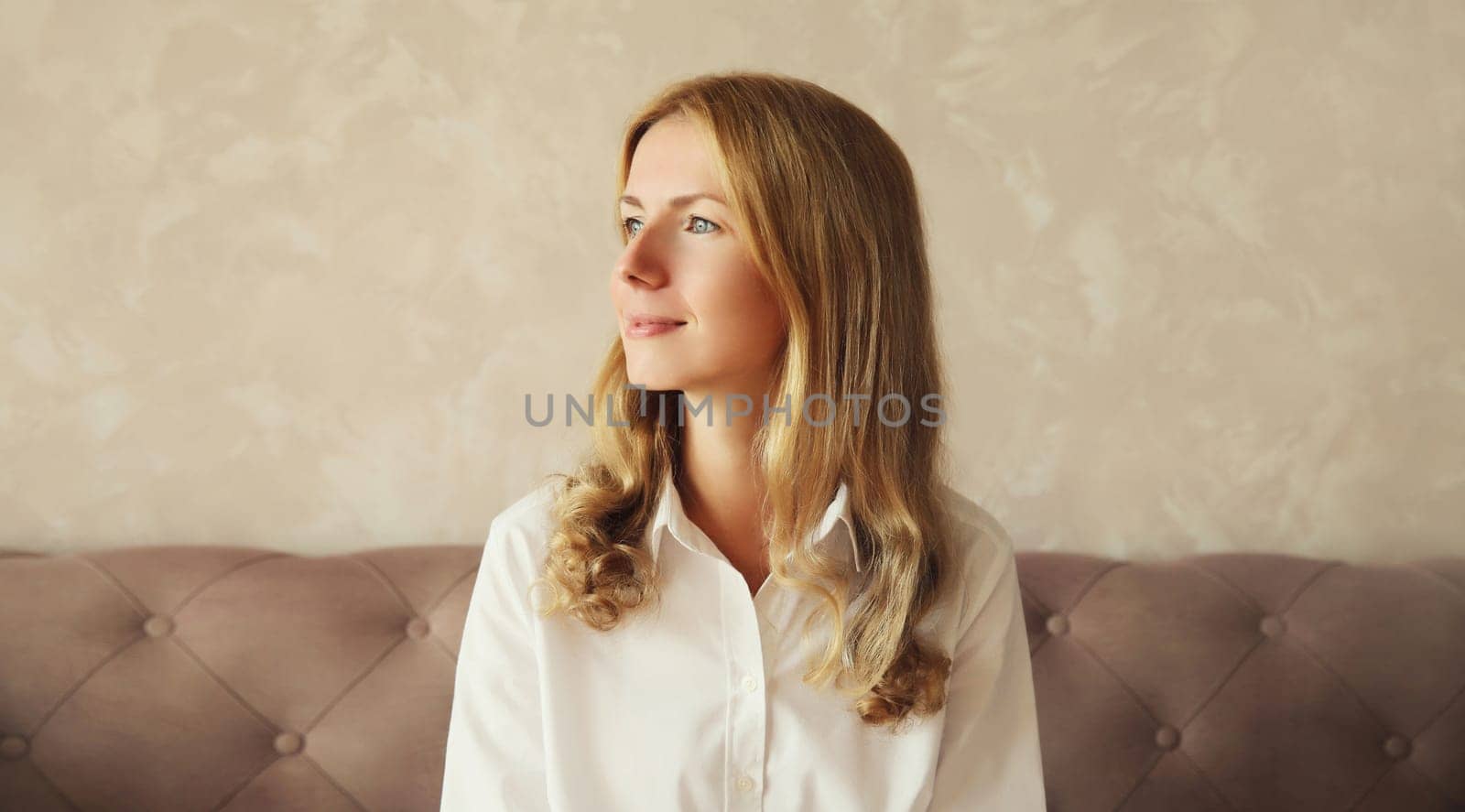 Happy satisfied young woman thinks looking out the window in early morning sitting on couch in the living room at home