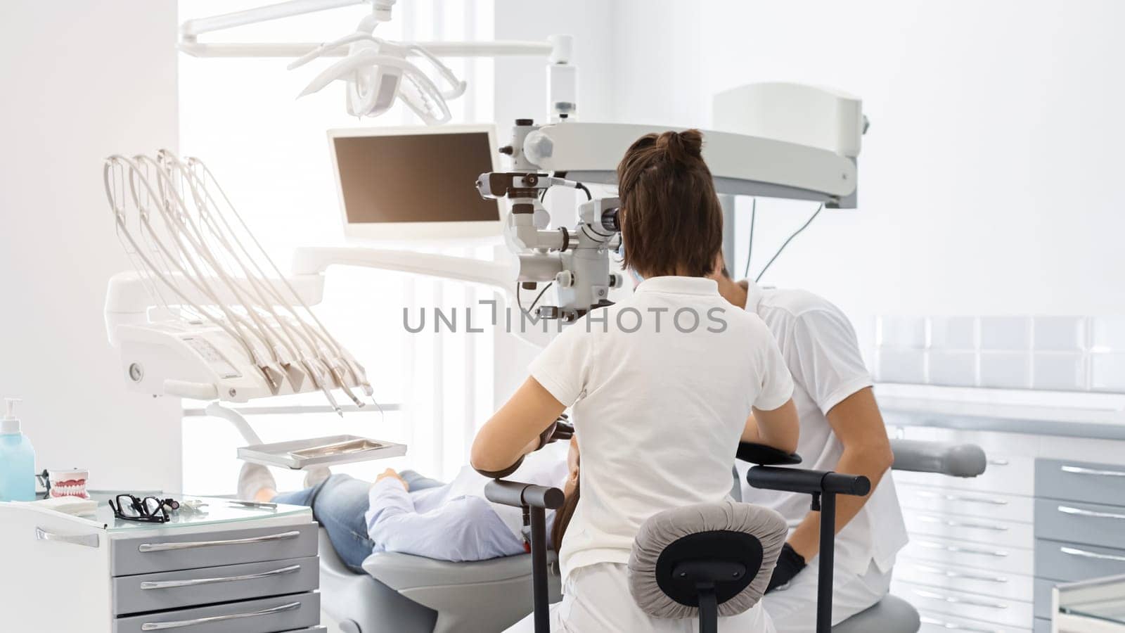 Rear view of two professional dentists giving treatment to patient, modern dental clinic interior, copy space