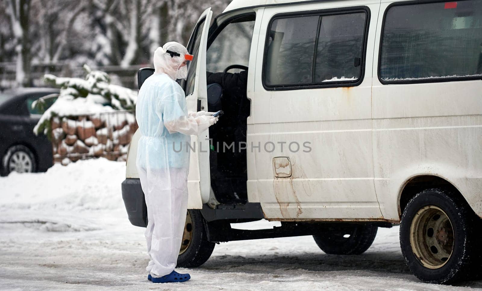 People in protective suits helping a sick person outdoors, coronavirus concept. Ambulance car.