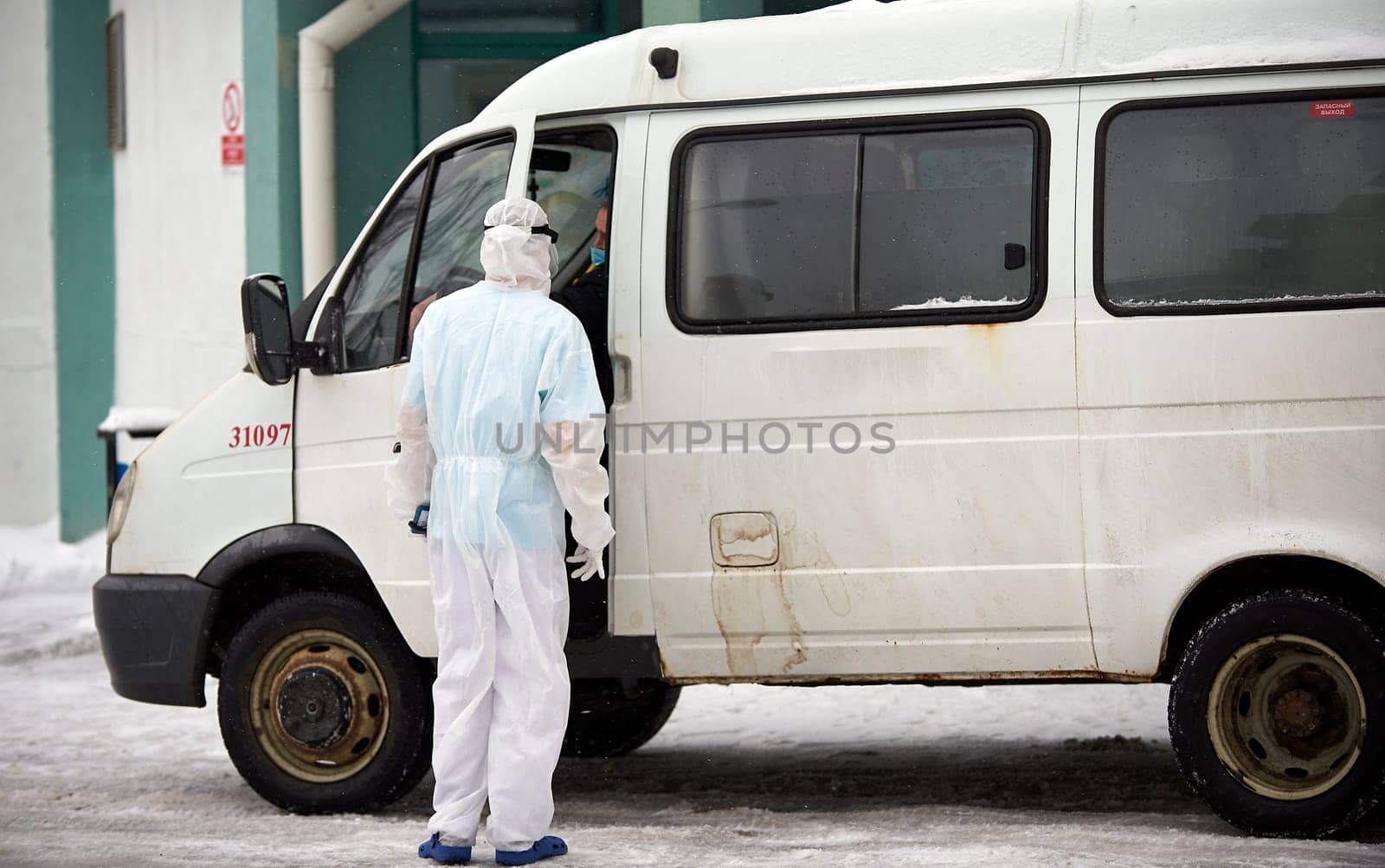 People in protective suits helping a sick person outdoors, coronavirus concept. Ambulance car.