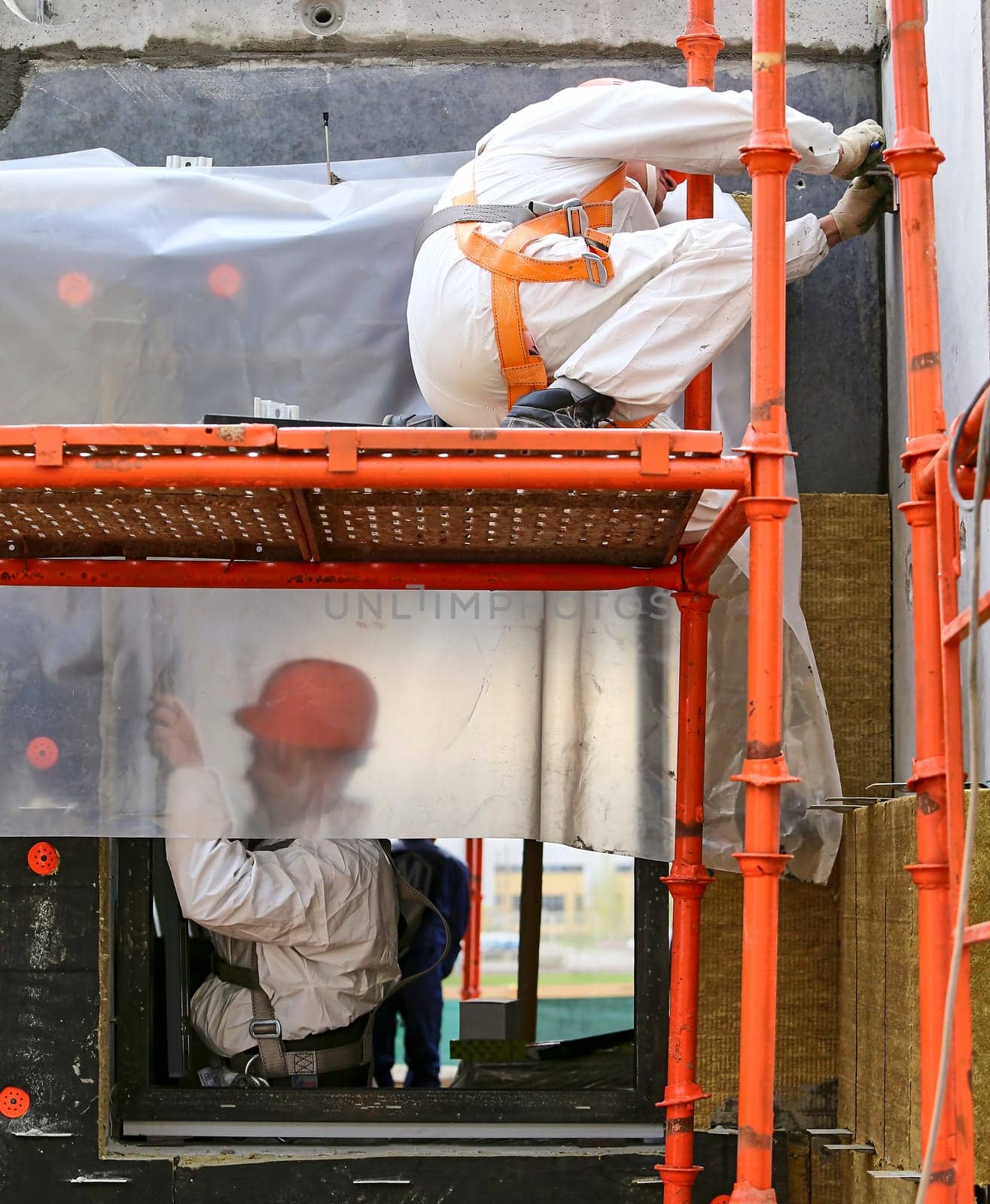 A builder measures the area wearing helmets, goggles and protective equipment at a construction site indoors. Installation of apartment insulation.